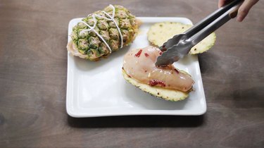 Placing chicken breast in between planks of pineapple skin