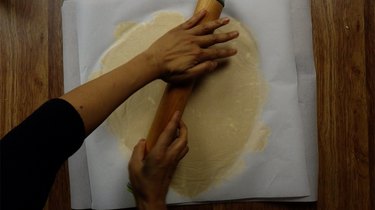 Rolling out gluten-free, low-carb coconut flour rolled pie crust between two pieces of parchment paper.